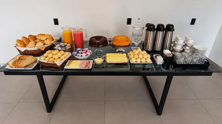 Mesa de café da manhã com pão, suco, bolos e café